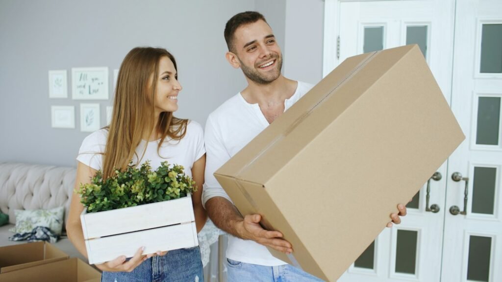 Couple carrying a large box and a house plant themselves on moving day